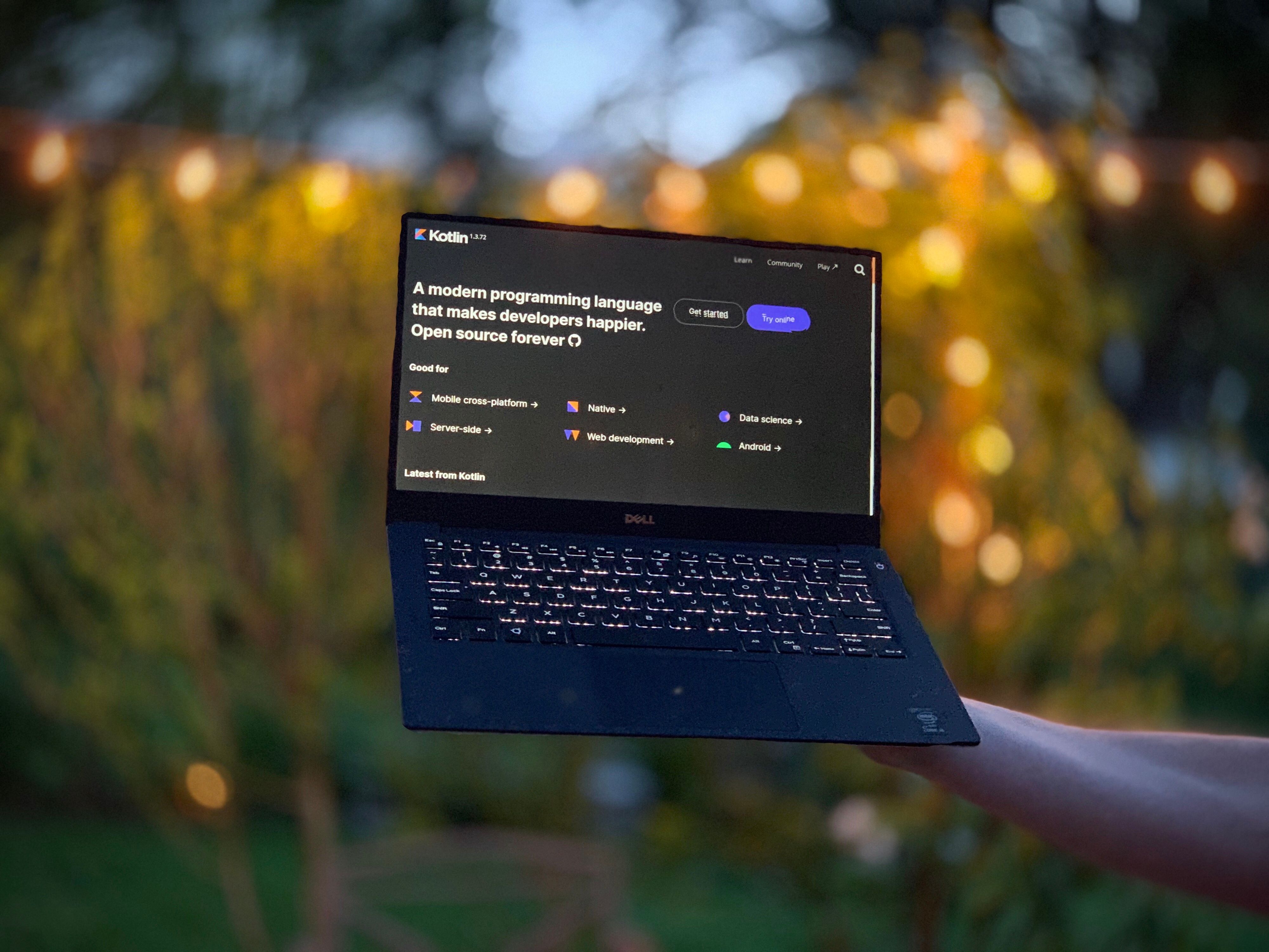 Holding up a laptop with blurred string lights as a backdrop. The laptop is displaying kotlin code from the Firefox Fenix peoject.